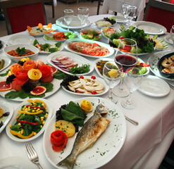 Grilled perch fish (Turkish: Levrek) with appetizer foods and red wine on the restaurant table.