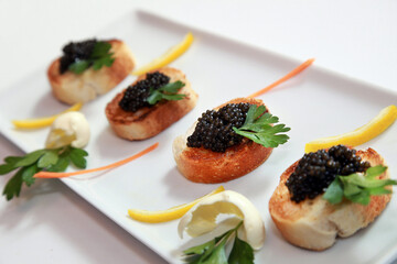 Black caviar appetizers and little toast with lemon slice on dinner plate.