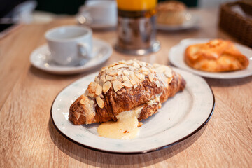A fresh large croissant on a beautiful plate in a cafe or restaurant. Close-up of a croissant and cream sprinkled with nuts. Sweet and delicious dessert for coffee time.