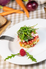 Tartare of fresh diced vegetables and salads in a white plate decorated with a raspberry
