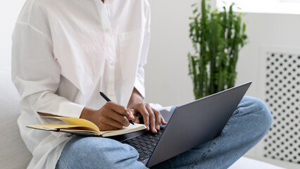 African american teenage girl making notes and holding laptop