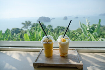 Mango smoothie put in glass on table Cafe sea island mountain background. 