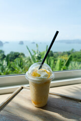 Mango smoothie put in glass on table Cafe sea island mountain background. 