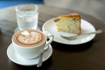 cup of hot coffee art with cake on wooden table in cafe