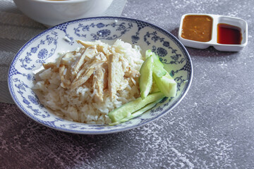 Rice Steamed With Chicken Soup Hainanese served in a Chinese style dish with soy sauce and broth on a gray table.