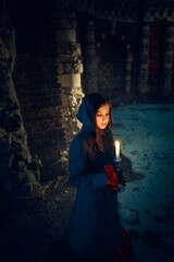 Fototapeta premium Girl with a candle near the dark castle stone wall in the night