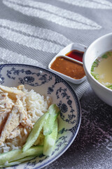Rice Steamed With Chicken Soup Hainanese served in a Chinese style dish with soy sauce and broth on a gray table.