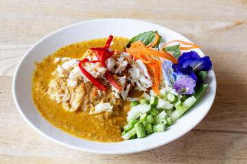 Crabmeat curry sauce with fermented rice noodle and side dishes in white plate on the wooden table. Ready to serve in the restaurant.