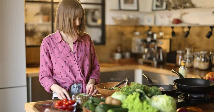 Young woman mixing salad and frying salmon steaks, cooking healthy food in the kitchen at home. Healthy lifestyle and wellness concept