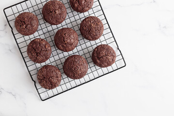 Freshly baked chocolate muffins on a grid on white table