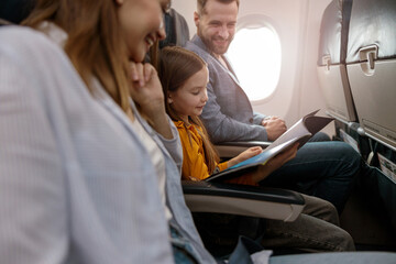 Little girl reading magazine with parents in airplane