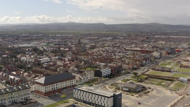 An aerial view of Rhyl promenade and seafront on a cloudy day, flying away from the town centre over the promenade, North Wales, UK