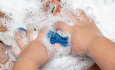 The boy washes the table with his hands with a rag.