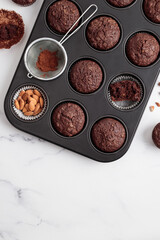 Freshly baked chocolate muffins in a baking pan on white table with ingredients