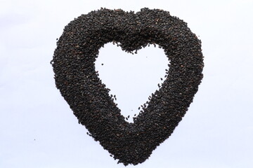 The sesame seeds piled on a white table are made into a heart shape as a concept of health and wellness. The organic sesame seed background arranged in a heart shape represents health care.