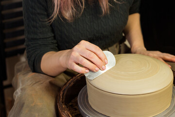 Potter's hands molds pot with tool close up. Woman works in pottery workshop. Clay bowl spinning on pottery wheel