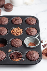 Freshly baked chocolate muffins in a baking pan on white table with ingredients