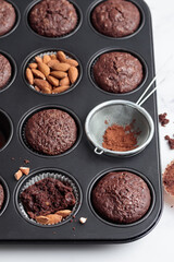 Freshly baked chocolate muffins in a baking pan on white table with ingredients