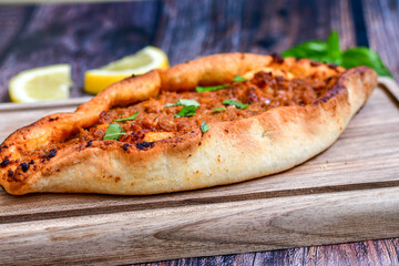 Traditional Turkish cuisine. Baked Pide dish with minced  beef, tomatoes and  herbs on  wooden background.  Turkish pizza pide