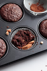 Freshly baked chocolate muffins in a baking pan on white table with ingredients