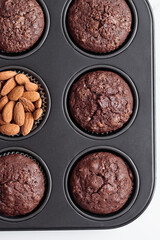 Freshly baked chocolate muffins in a baking pan on white table with ingredients