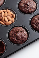 Freshly baked chocolate muffins in a baking pan on white table with ingredients