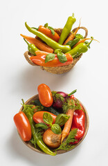 Traditional wooden plate and basket with fresh seasonal vegetables: green pepper, tomato, onion, carrot, cucumber, basil, dill on white background, top view, stock photo