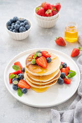 A stack of delicious fluffy pancakes with berries and honey on a white plate on a gray concrete background. Copy space.