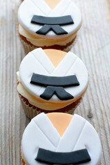 Three little cakes are lying on the wooden background. Cakes in white clothes with black belts. Karate clothes on the cakes © Anastasia Pestova