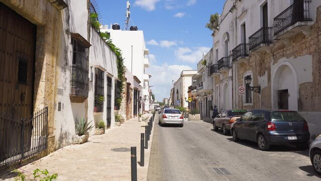 Santo Domingo, Dominican Republic - March 16, 2022. Summer walk through the ancient tropical city. Sunny streets are decorated with plants. Bright blue sky over white buildings. Dominican holidays.