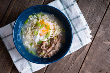 a blue bowl of gyudon ramen with egg and onion leeks