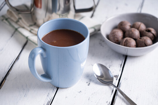 a mug of hot chocolate with tablea on the side on white wood background