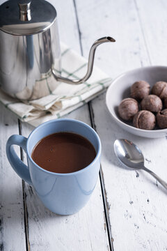 a mug of hot chocolate with tablea on the side on white wood background