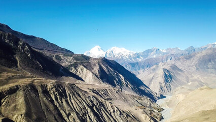 A panoramic view on dry Himalayan landscape. Located in Mustang region, Annapurna Circuit Trek in Nepal. In the back there is snow capped Dhaulagiri I. Barren and steep slopes. Harsh condition.