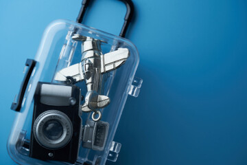 Toy airplane and camera inside a transparent luggage against blue background