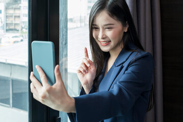 Young businesswoman using smartphone working in hotel room during her business travel. Businesswoman working from hotel room on business trip standing by the window in sunny day.