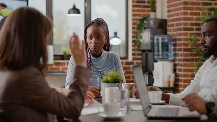 Close up of employee talking to colleagues about business project development in startup office. Woman explaining marketing stratgy, brainstorming ideas to plan data presentation.