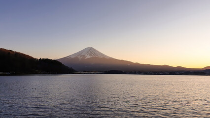 Idyllic view on Mt Fuji from the side of Kawaguchiko Lake, Japan. The mountain is surrounded by clouds. Calm surface of the lake moved by gentle wind. Serenity and calmness. Soft colors of the sunset