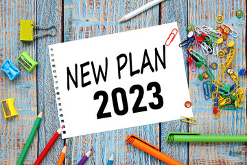 NEW PLAN 2023. text on paper from a notepad on a blue wooden background near colorful stationery