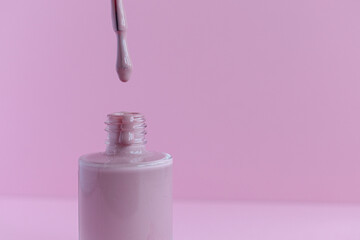 Pink nail polish on a pink background. Mani Pedi. Open varnish. Manicure. A drop of varnish drips from the brush. Lacquer advertisement. Close-up photo from the side.