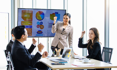 Happy excited cheerful Asian professional successful businessman businesswoman team colleagues in formal suit sitting standing in meeting room holding fists up celebrating job achievement together