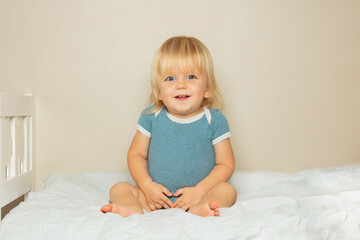 Fototapeta premium Smiling blond toddler boy sit on the bed in nursery