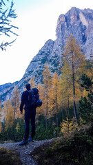 Naklejka na ściany i meble A man with big hiking backpack standing on the bottom of the valley of Lienz Dolomites, Austria, looking at the immense mountain in front of him. Wandering in the Alps.Admiring beauty of the nature