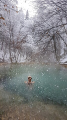A girl in a hat swimming in a natural thermic spring in Maibachl, Austria during snowfall, winter. The thermic pool is located in the middle of the forest. Healing power of natural water. Relaxation