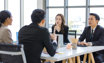 Asian young professional successful businesswoman and businessman employee in formal suit sitting at working desk negotiating discussing with unrecognizable male and female customers in meeting room