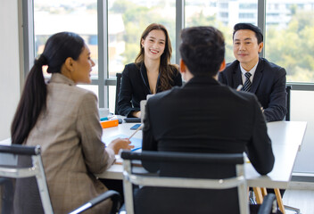 Asian young professional successful businesswoman and businessman employee in formal suit sitting at working desk negotiating discussing with unrecognizable male and female customers in meeting room