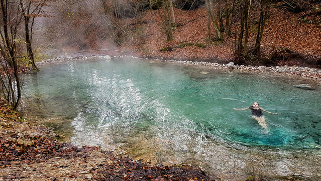 A girl in a black swimsuit swimming in a natural thermic spring in Maibachl, Austria during autumn. The thermic pool is located in the middle of the forest. Healing power of natural water. Relaxation