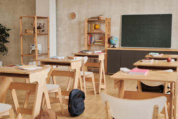 Background image of modern school classroom with wooden desks in row facing blackboard, no people, copy space