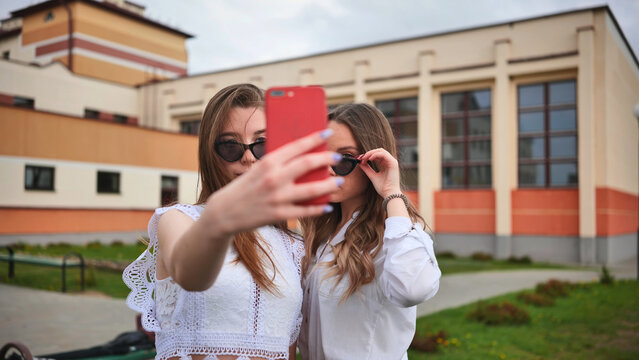 Two girls schoolgirls make a selfie using a smartphone against the background of the school.