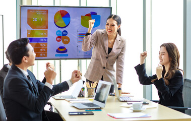 Happy excited cheerful Asian professional successful businessman businesswoman team colleagues in formal suit sitting standing in meeting room holding fists up celebrating job achievement together